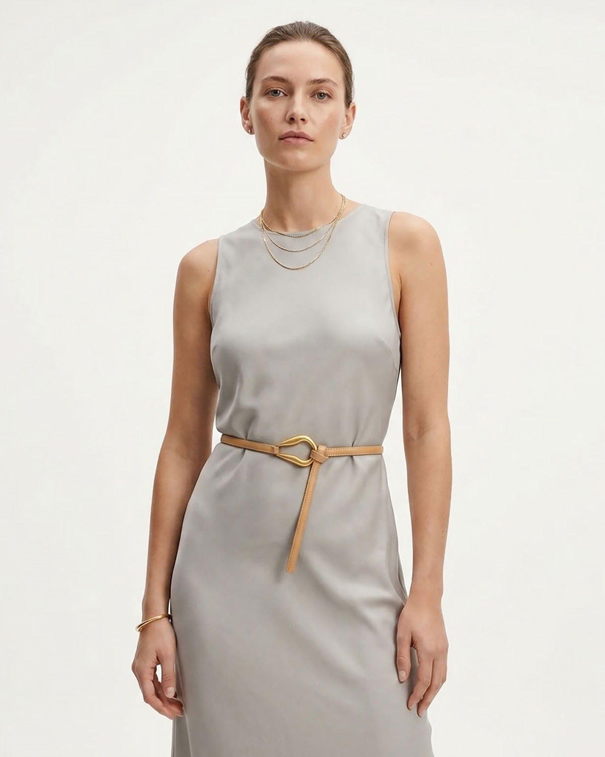 A woman modeling a sleeveless light gray dress with an Apricot Slim Knotted Leather Belt with Gold Loop