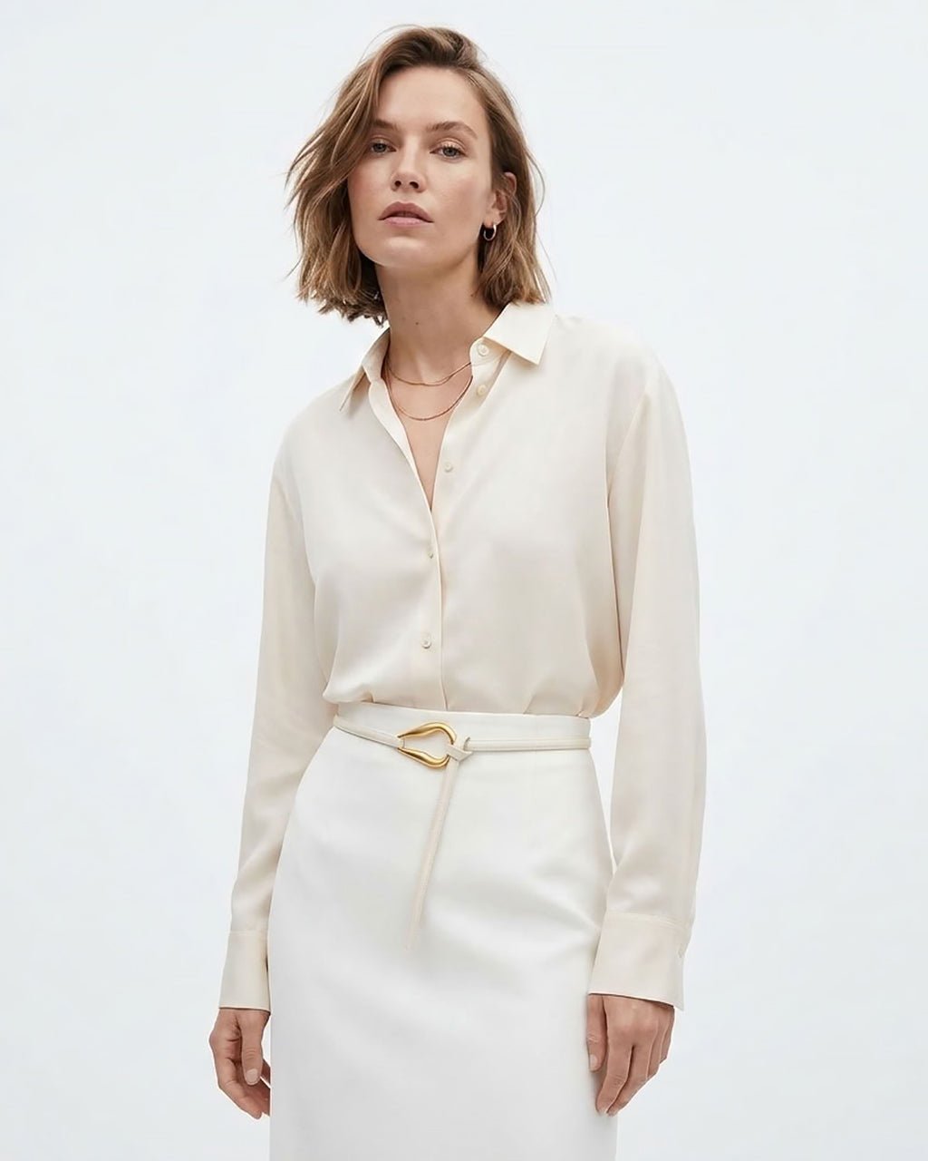 A woman modeling a cream-colored long-sleeve button-up shirt tucked into a matching cream skirt with a White Slim Knotted Leather Belt with a gold-toned loop hook Buckle