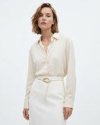 A woman modeling a cream-colored long-sleeve button-up shirt tucked into a matching cream skirt with a White Slim Knotted Leather Belt with a gold-toned loop hook Buckle