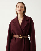 A woman in a burgundy coat with a leather caramel-colored belt with a sculptural gold-toned hook clasp by BUCKLE Collective