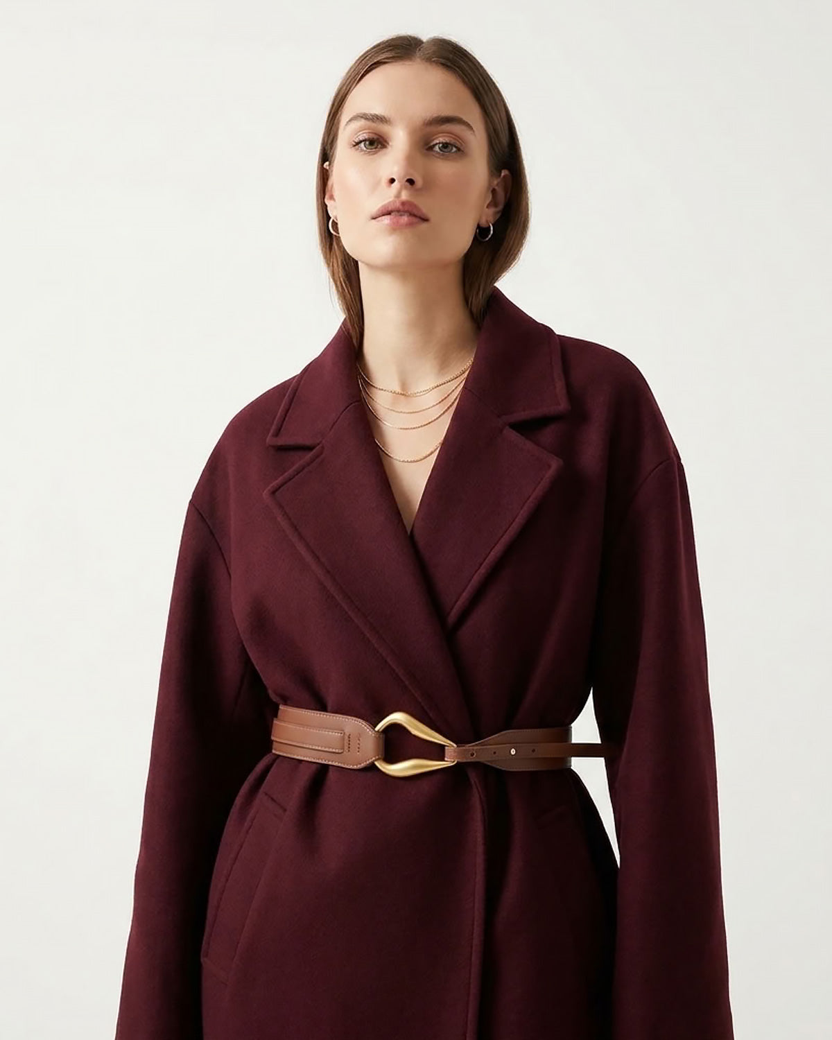 A woman in a burgundy coat with a leather caramel-colored belt with a sculptural gold-toned hook clasp by BUCKLE Collective