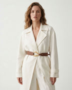 A woman wearing a cream-colored wrap coat with a Caramel-colored Leather Belt with a sculptural gold-toned hook clasp by BUCKLE Collective
