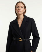 A woman wearing a black coat with a Black Leather Belt with a sculptural gold-toned hook clasp by BUCKLE Collective
