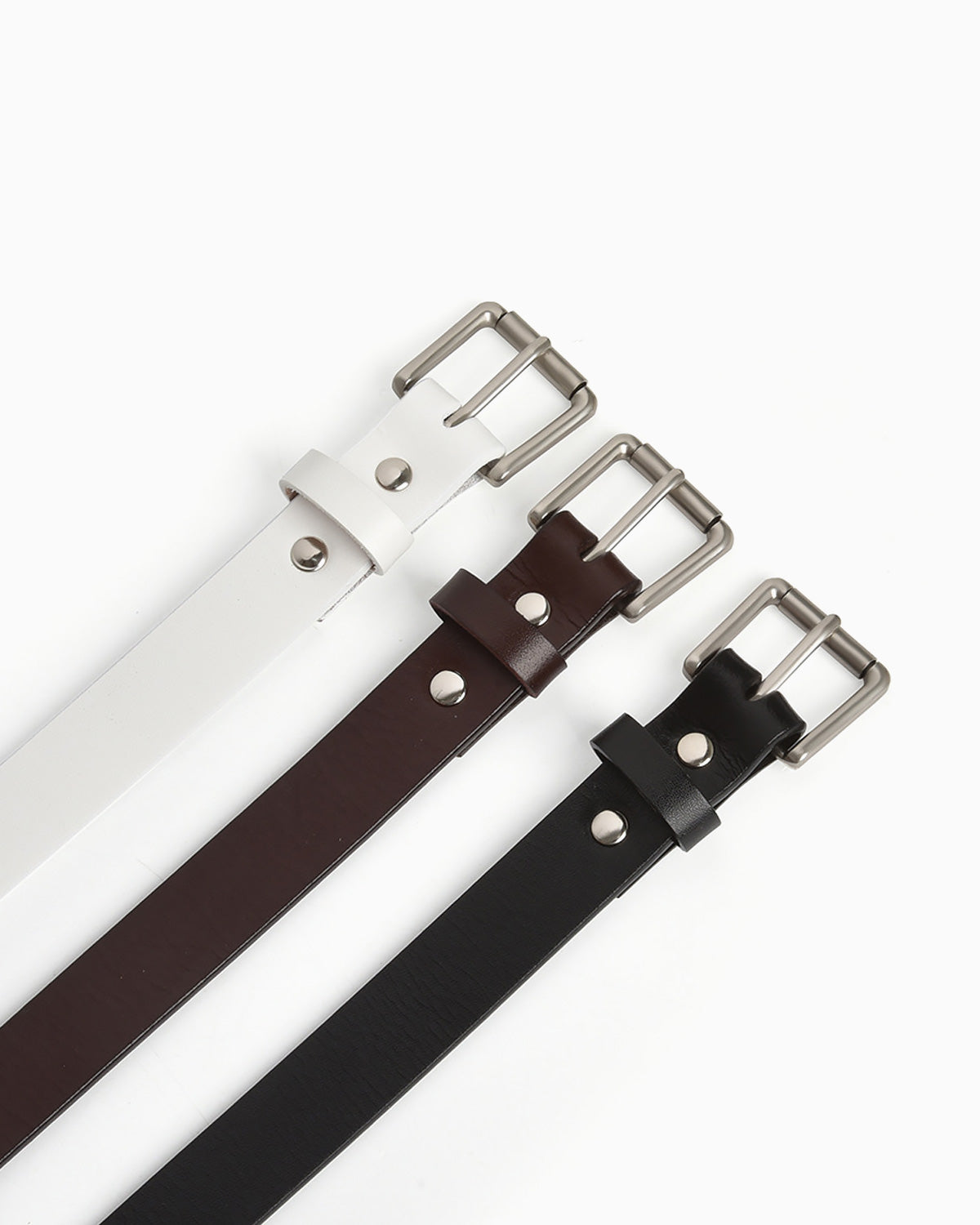 Three leather belts in white, coffee-brown, and black, arranged diagonally on a clean white background. Each belt features a silver-tone metal buckle and matching metal rivets | BUCKLE Collective
