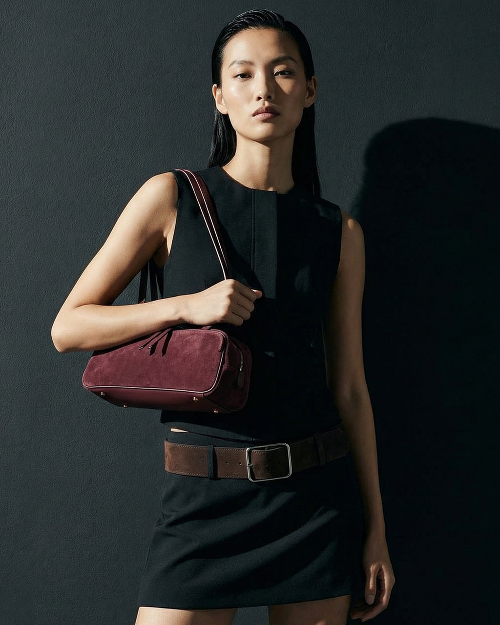 A woman in a stylish, chic outfit with a wide suede belt carries a Minimalist Suede Boston Burgundy Color Handbag with Gold Details