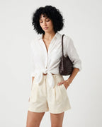 A woman modeling a white long-sleeve button-up shirt tied at the waist and cream-colored shorts, carrying a coffee-colored Genuine Leather Woven Shoulder Bag