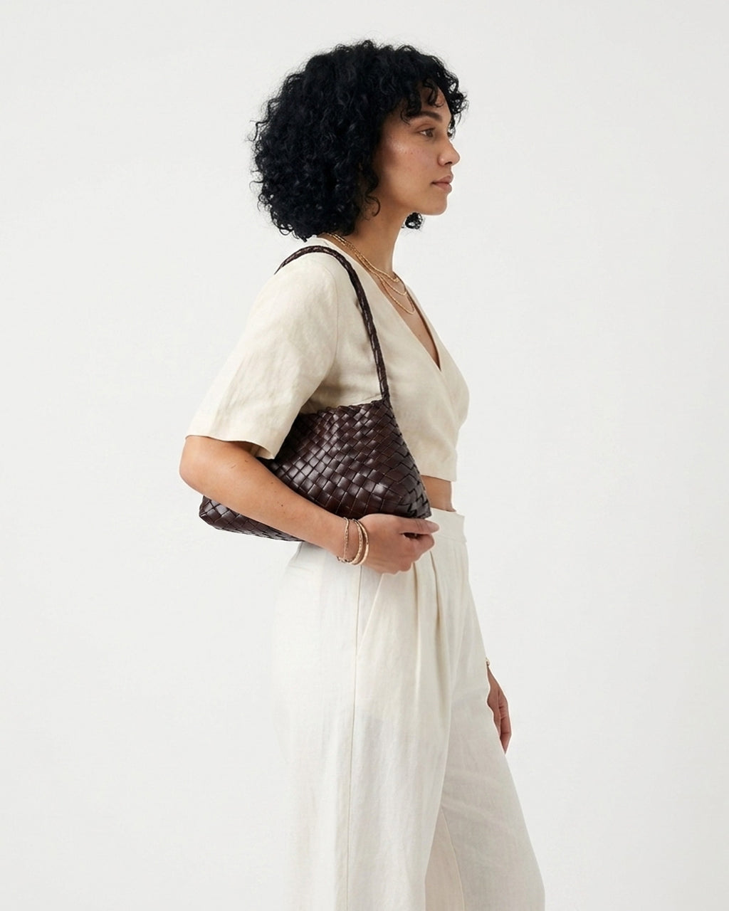 A woman in a cream-colored linen outfit is shown from the side, carrying a coffee-colored Genuine Buffalo Leather Woven Shoulder Bag