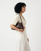 A woman in a cream-colored linen outfit is shown from the side, carrying a coffee-colored Genuine Buffalo Leather Woven Shoulder Bag