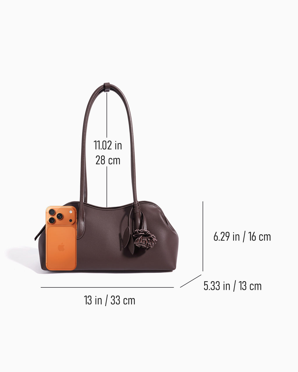 A dark brown leather handbag shown on a light gray background with overlaid dimension lines and measurements for width, height, and handle length. A small orange phone is shown next to the bag for scale.
