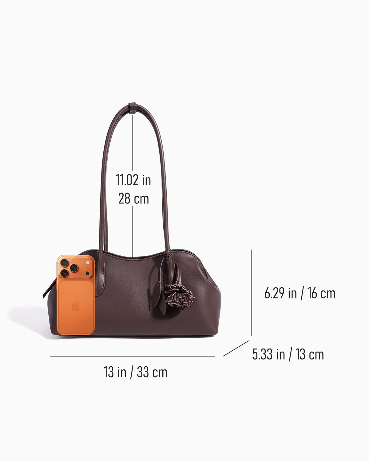 A dark brown leather handbag shown on a light gray background with overlaid dimension lines and measurements for width, height, and handle length. A small orange phone is shown next to the bag for scale.