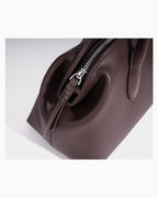 A close-up of a dark brown leather handbag showing the side profile, a silver zipper with a decorative pull, and a leather strap detail