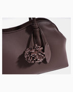A close-up of a coffee-colored leather handbag featuring a decorative matching leather tassel charm and small leather tags
