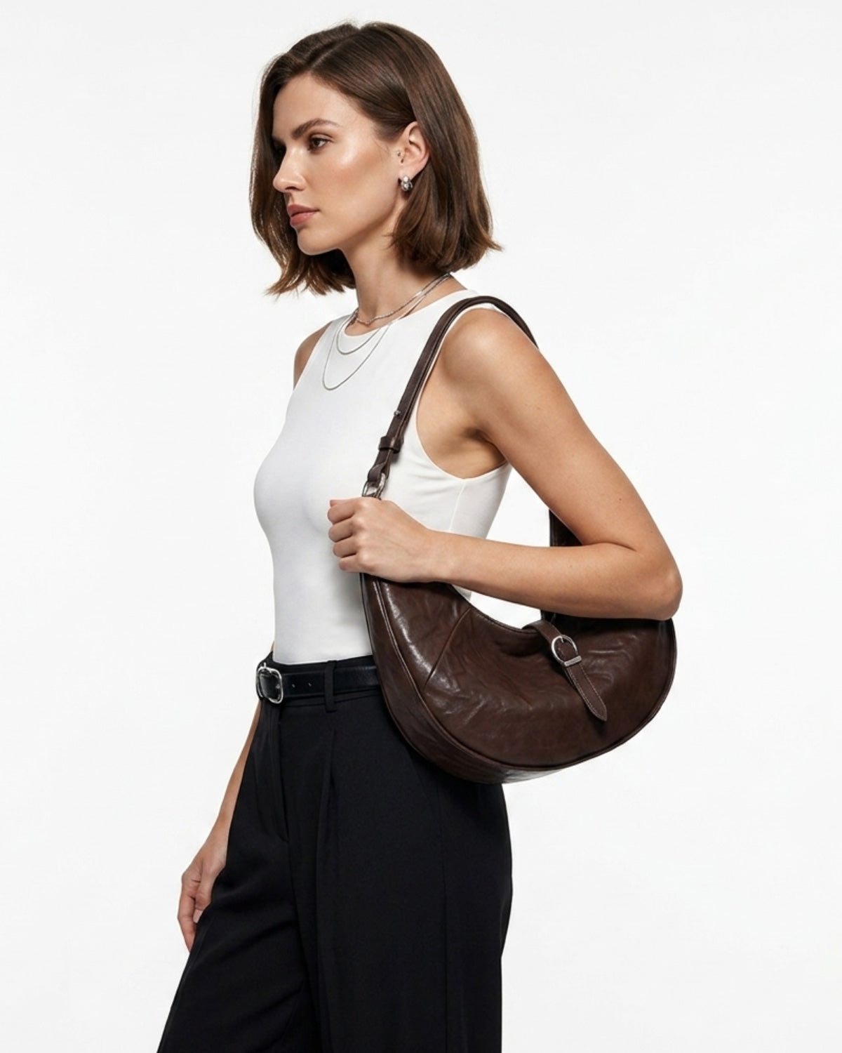 A stylish woman in a sleek summer outfit carries a Coffee Color Leather Dumpling Bag with Adjustable Strap & Buckle Accent