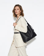 A stylish woman in a white fashion-forward outfit carries a Black Genuine Leather Tote Bag with an Adjustable Strap