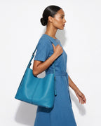 A stylish woman in a blue casual dress carries a Blue Genuine Leather Tote Bag with an Adjustable Strap and Inner Pouch