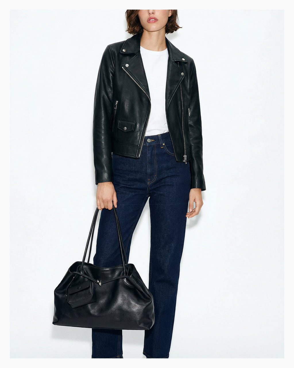 A chic woman in a cool casual outfit holds a versatile leather tote shoulder bag with a matching pouch in black color