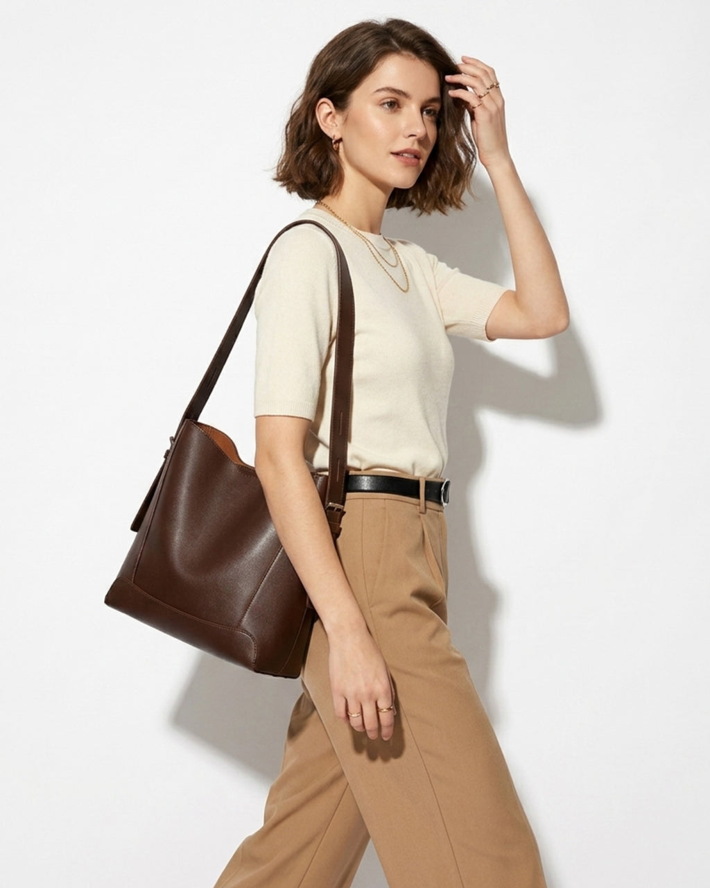 A woman in a stylish casual outfit carries a Genuine Nappa Leather Minimalist Versatile Structured Bucket Bag in Coffee Color
