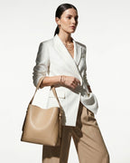 A stylish, confident woman in a polished light outfit carries a Genuine Leather Minimalist Versatile Structured Bucket Bag in Beige color
