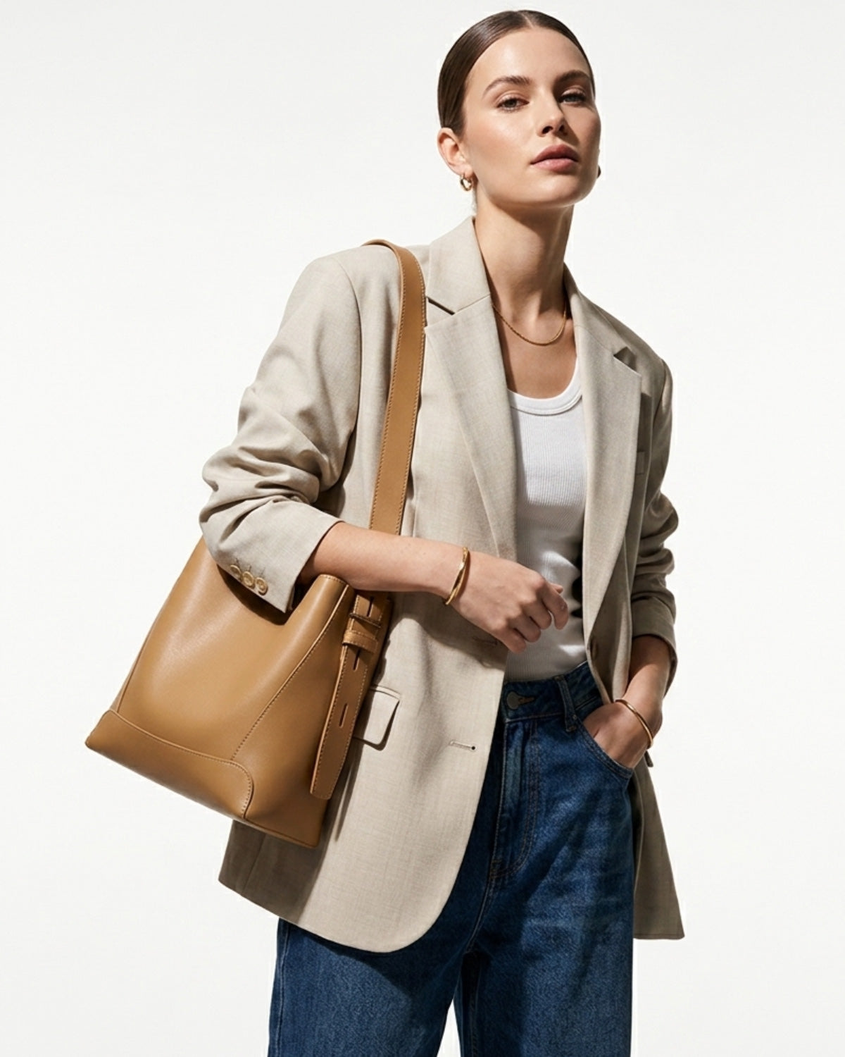 A woman in a casual outfit carries a stylish and spacious Structured Genuine Leather Bucket Bag in Caramel Color