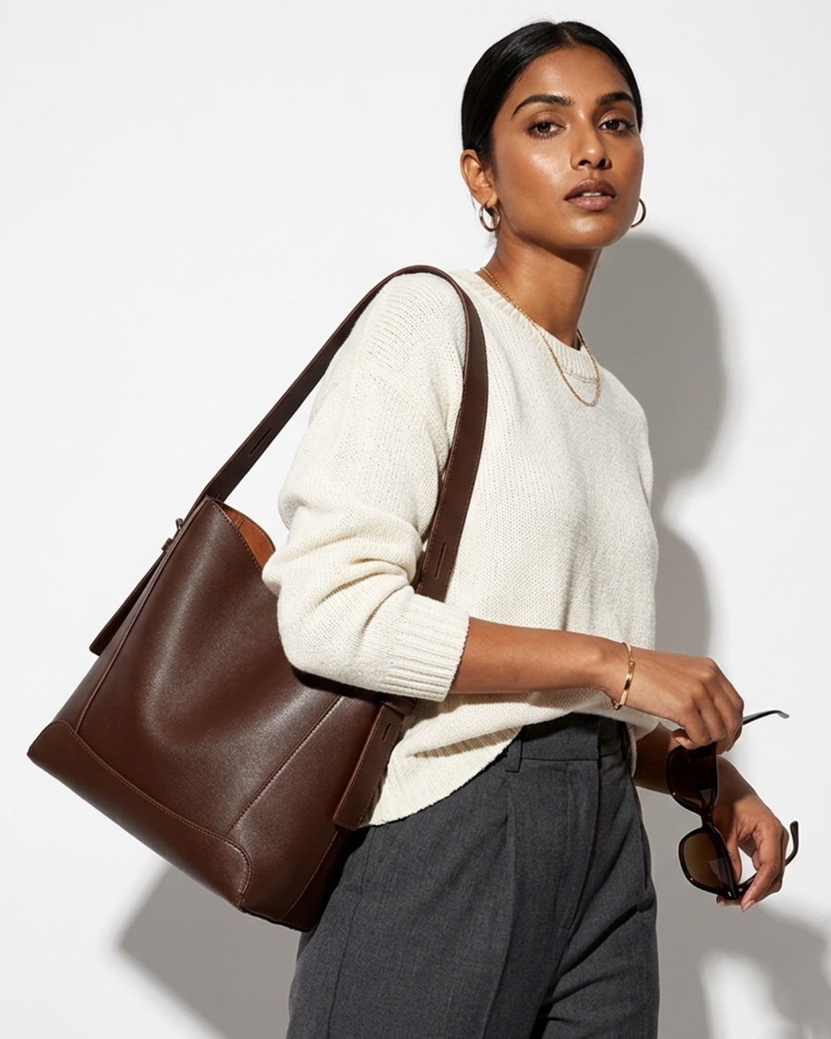 A woman in a stylish casual outfit carries a Genuine Leather Minimalist Versatile Structured Bucket Bag in Coffee Color