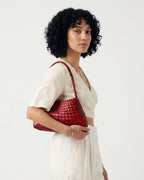A woman with short curly black hair models a red woven leather shoulder bag