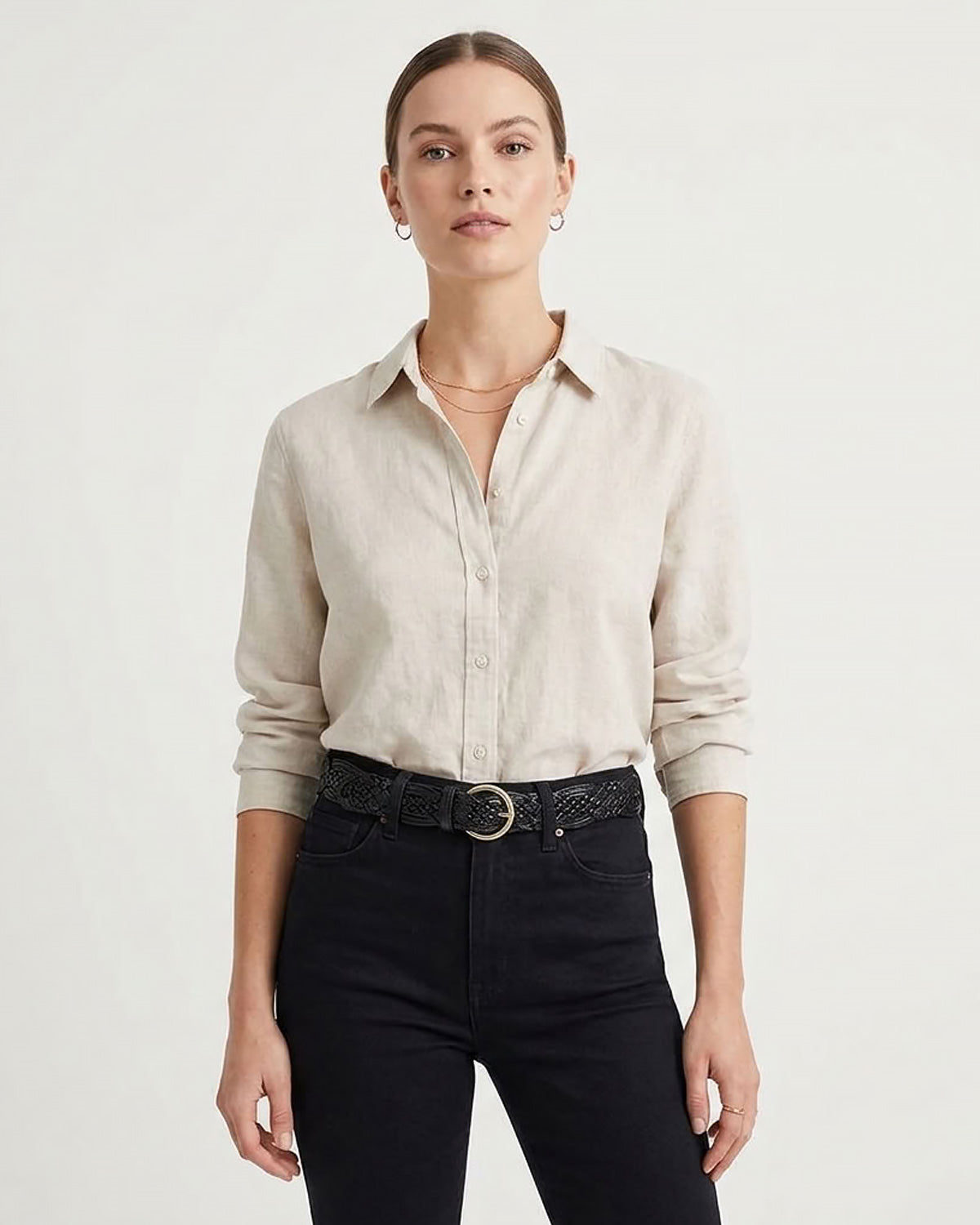 A woman in a light beige linen button-down shirt tucked into black jeans with a black woven belt with a gold-toned circular buckle | BUCKLE Collective