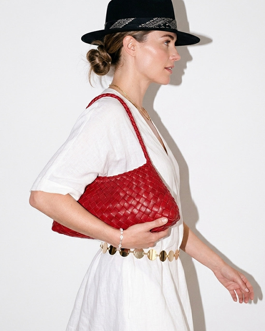 A woman in a relaxed, stylish summer outfit with hat and chain belt carries a Red Vegan Leather Woven Shoulder Bag