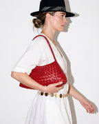 A woman in a relaxed, stylish summer outfit with hat and chain belt carries a Red Vegan Leather Woven Shoulder Bag