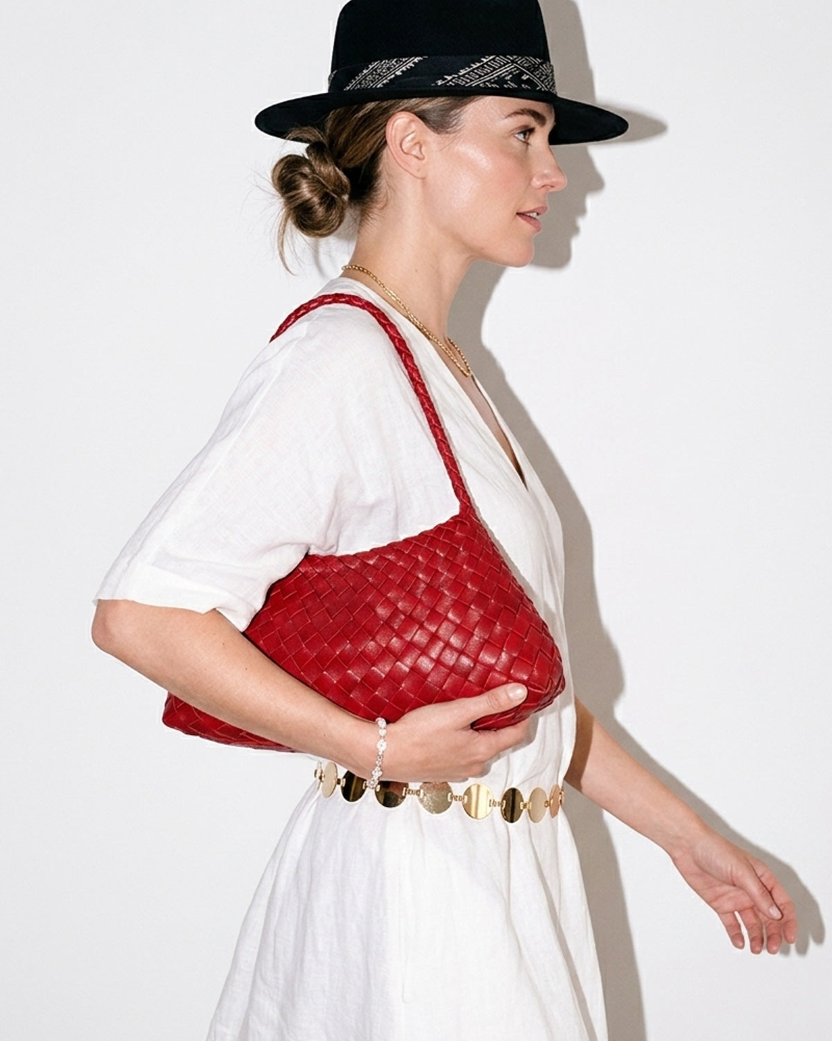 A woman in a relaxed, stylish summer outfit with hat and chain belt carries a Red Vegan Leather Woven Shoulder Bag