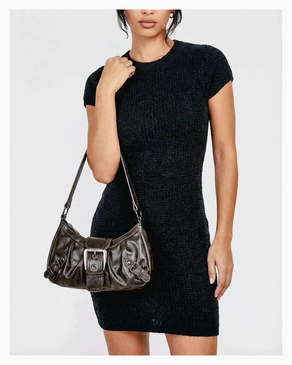 A woman in a chic knitted black dress with a trendy Y2K vegan leather shoulder coffee-color bag with buckle detail