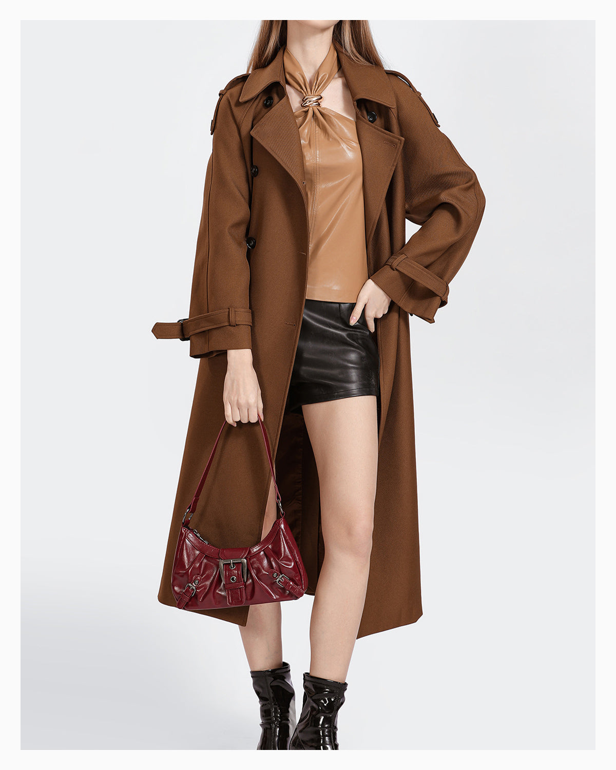 A woman in a brown coat and black shorts with a trendy vegan leather shoulder dark red bag with buckle details