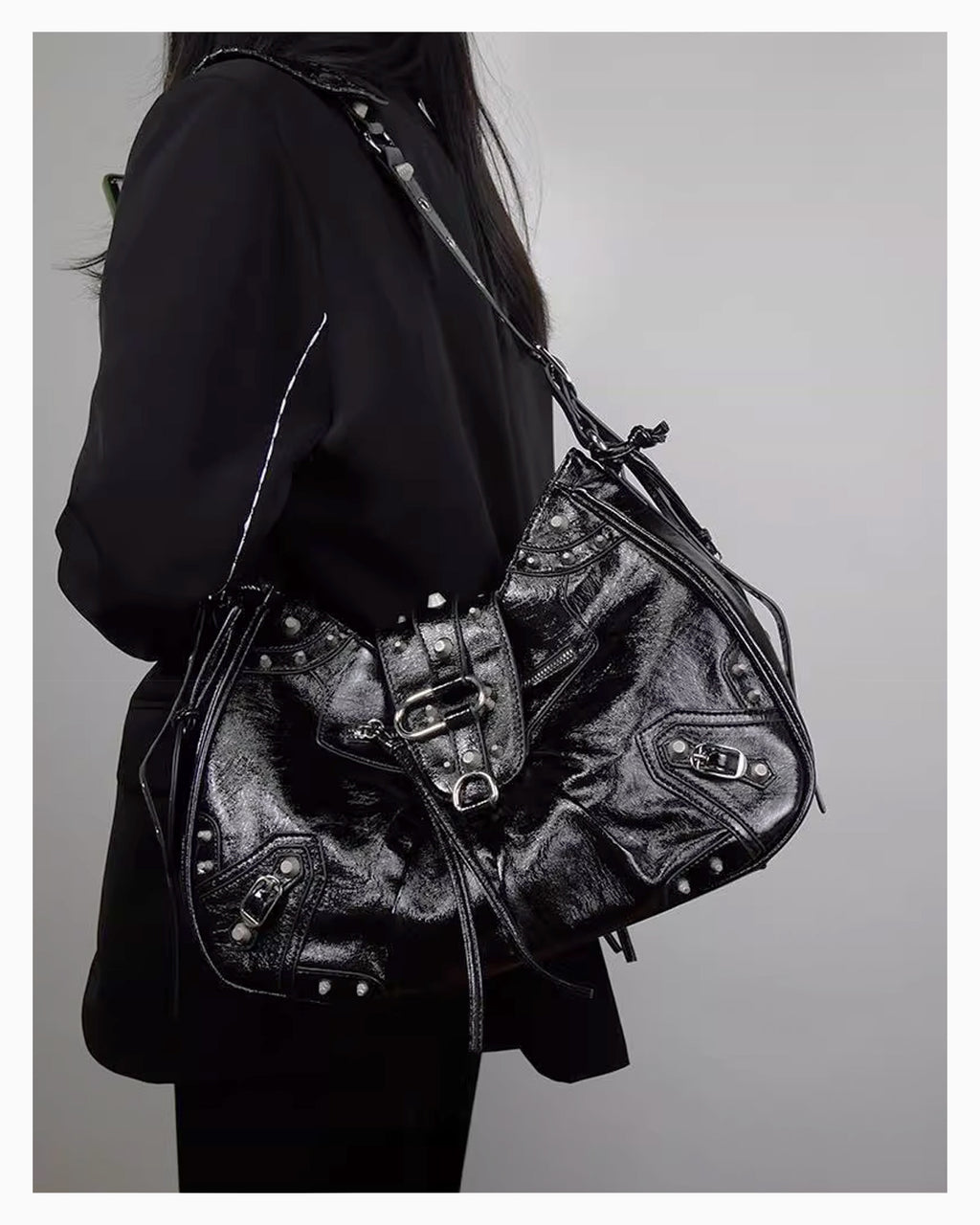 A woman in a black coat wearing a Black Studded Y2K Statement Vegan Leather Handbag with riveted strap, buckles, and an adjustable single strap