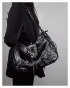 A woman in a black coat wearing a Black Studded Y2K Statement Vegan Leather Handbag with riveted strap, buckles, and an adjustable single strap