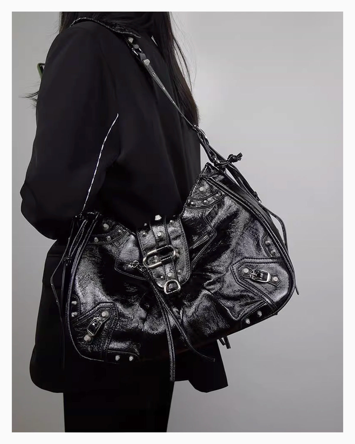 A woman in a black coat wearing a Black Studded Y2K Statement Vegan Leather Handbag with riveted strap, buckles, and an adjustable single strap