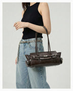 A woman in a chic casual outfit carries a Genuine Leather Shoulder Baguette Bag with zippered side pockets and turn-lock closure in Havana Color