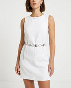 A woman wearing a sleeveless white linen dress with a silver chain belt featuring circular metal accents | BUCKLE Collective
