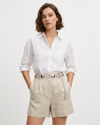 A woman modeling a white long-sleeve button-up shirt and light beige linen shorts with a silver disc-ring chain belt | BUCKLE Collective