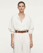 A model wearing a white long-sleeve collared shirt and matching white wide-leg trousers, styled with a caramel-colored Genuine Suede Leather Belt with Silver Rectangular Buckle and layered gold necklaces