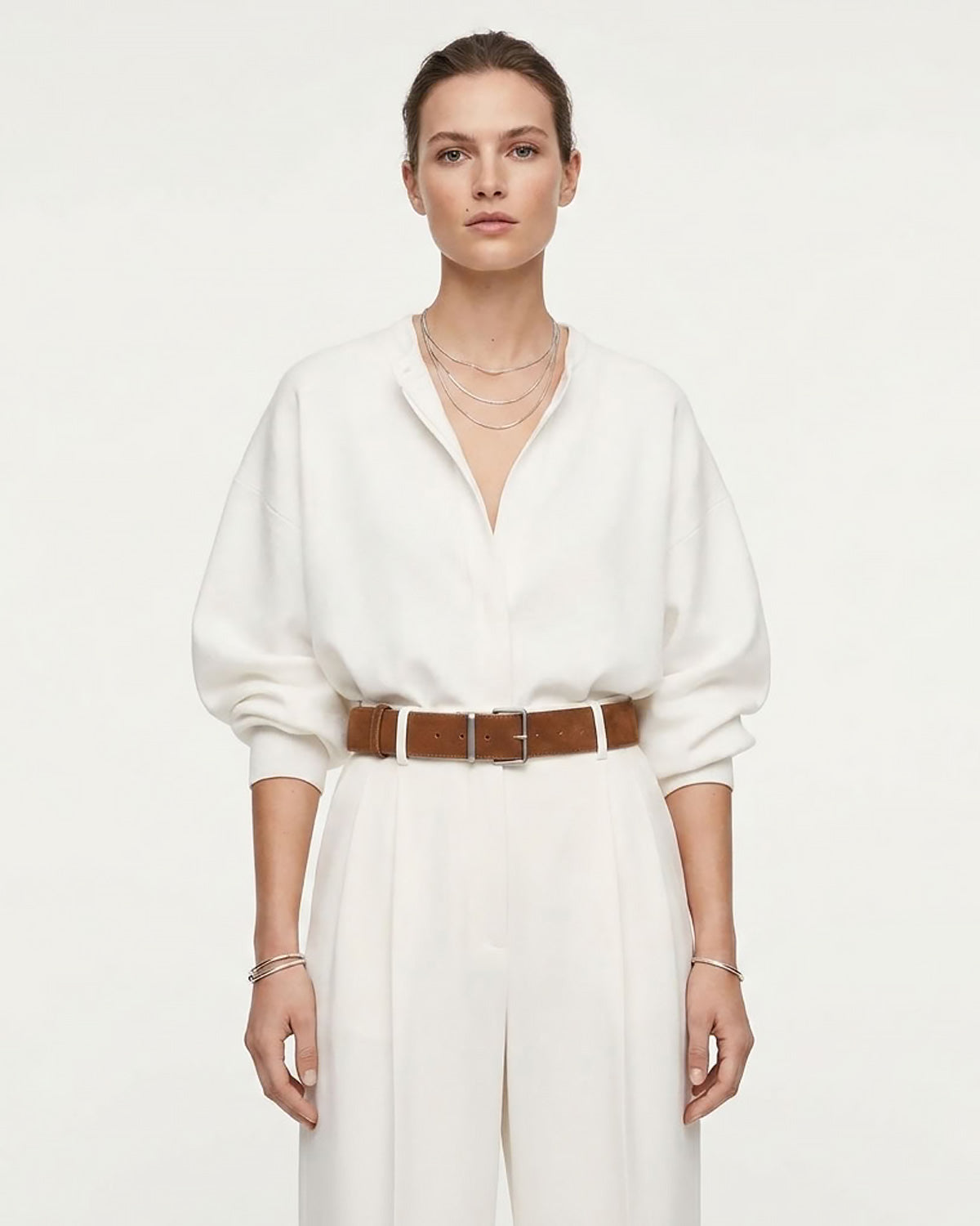 A model wearing a white long-sleeve collared shirt and matching white wide-leg trousers, styled with a caramel-colored Genuine Suede Leather Belt with Silver Rectangular Buckle and layered gold necklaces