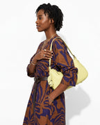 A woman in a stylish brown-purple pattern dress holding a Genuine Leather Crescent Baguette Shoulder Bag in a Custard Yellow Color
