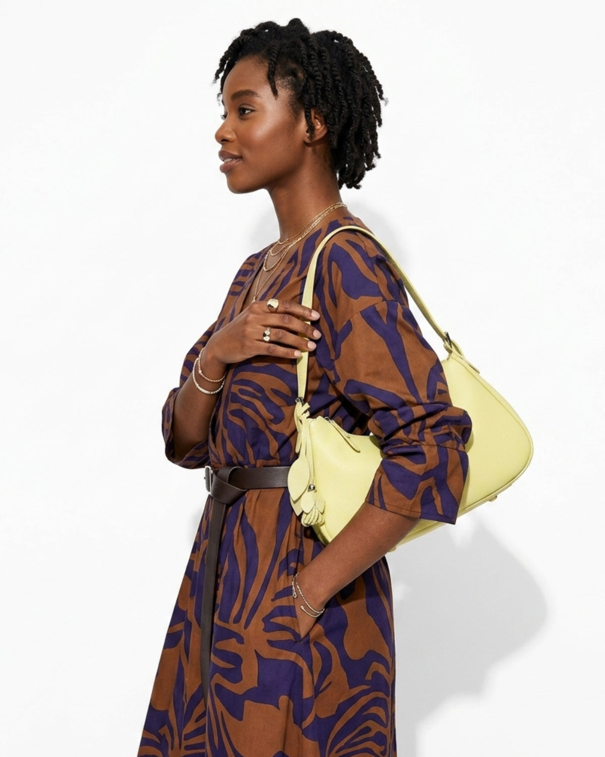 A woman in a stylish brown-purple pattern dress holding a Genuine Leather Crescent Baguette Shoulder Bag in a Custard Yellow Color