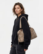 A woman wearing a black hoodie and dark jeans carries a Versatile Studded Shopper Tote Bag