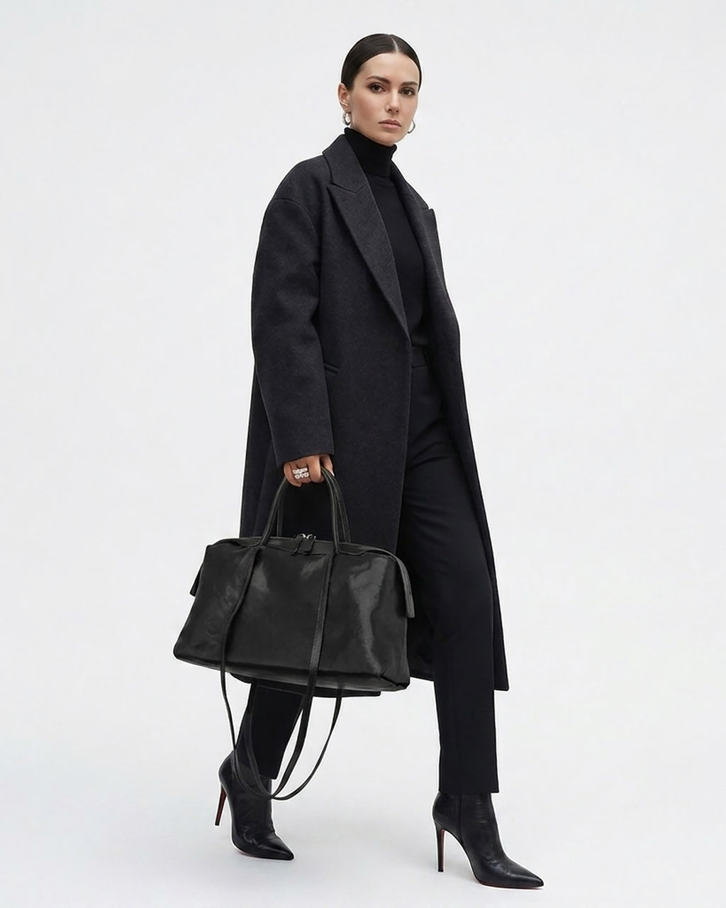 A model wearing a long black coat, black turtleneck, and black trousers, holding a black leather duffel bag | BUCKLE Collective