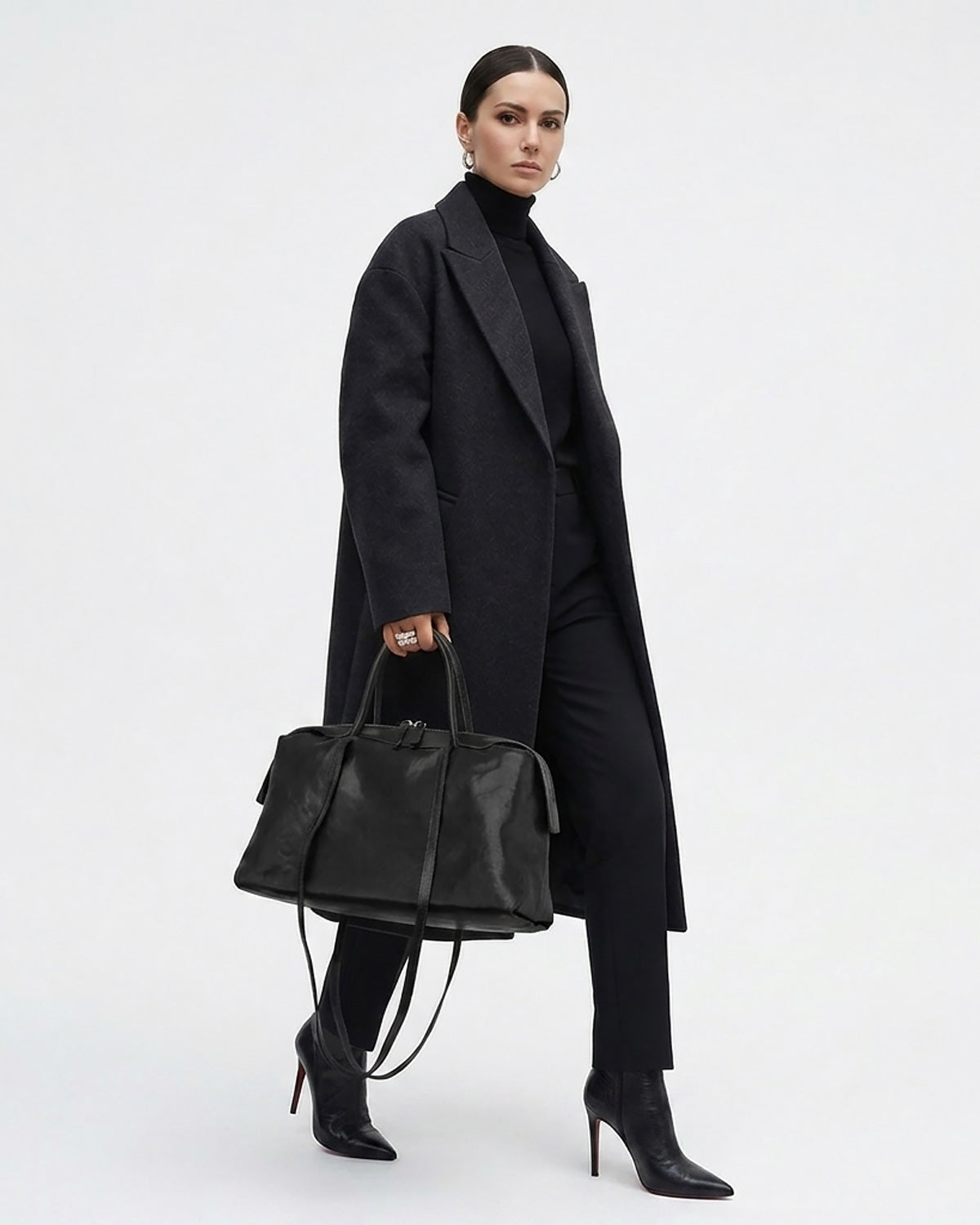 A model wearing a long black coat, black turtleneck, and black trousers, holding a black leather duffel bag | BUCKLE Collective