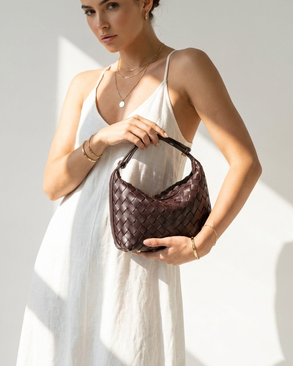 A woman in a light white summer dress holds a Faux Vegan Leather Woven HOBO Handbag with an adjustable strap in purple grape color