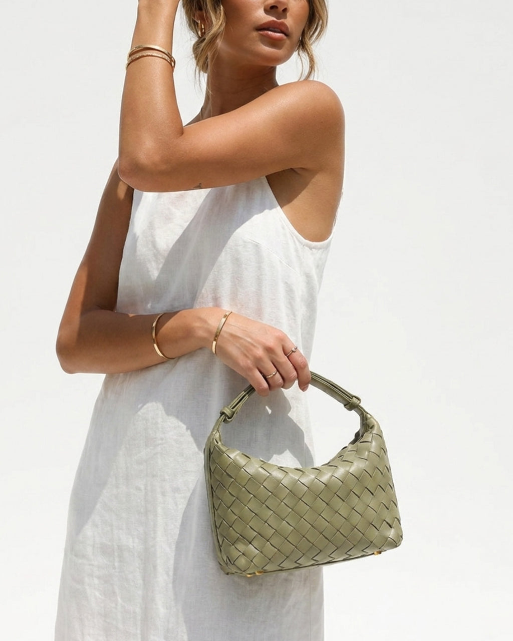 A stylish woman in a white summer dress holds a trendy Faux Vegan Leather Woven HOBO Handbag in travertine color