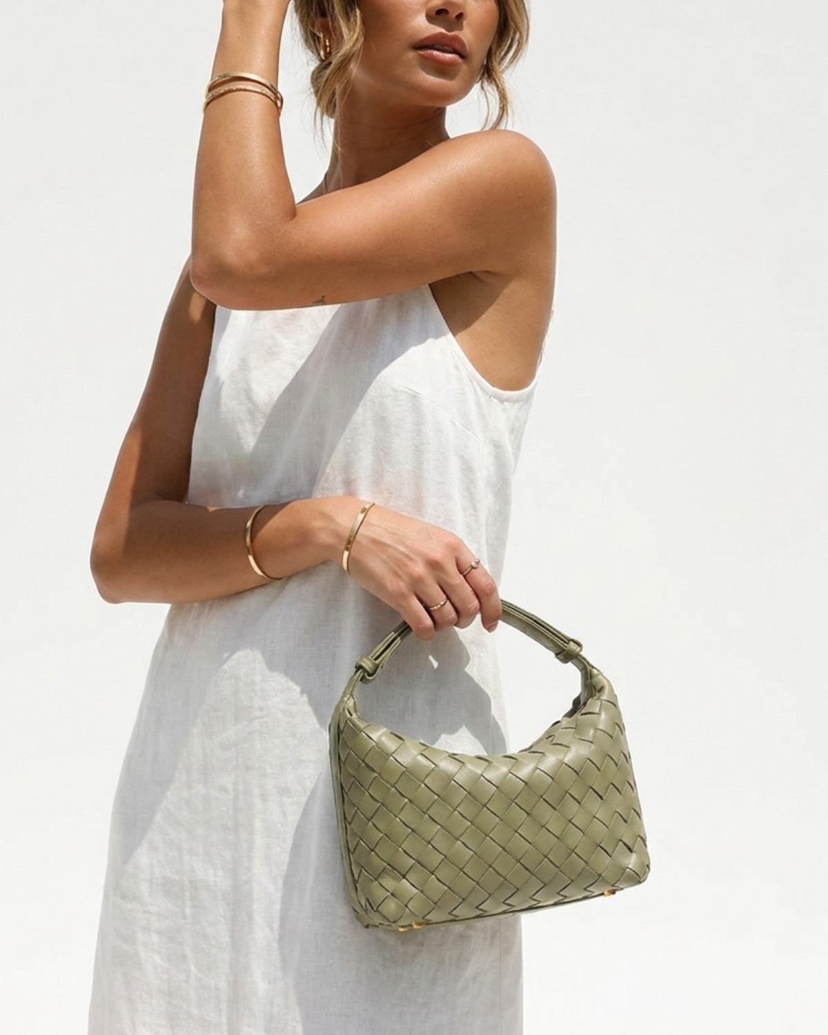 A stylish woman in a white summer dress holds a trendy Faux Vegan Leather Woven HOBO Handbag in travertine color