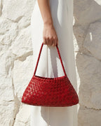 A woman in a white dress carries a Red Vegan Leather Woven Shoulder Bag