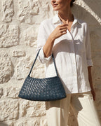 A woman in a casual summer outfit carries a trendy Vegan Faux Leather Woven Shoulder Bag in Victoria Blue Color