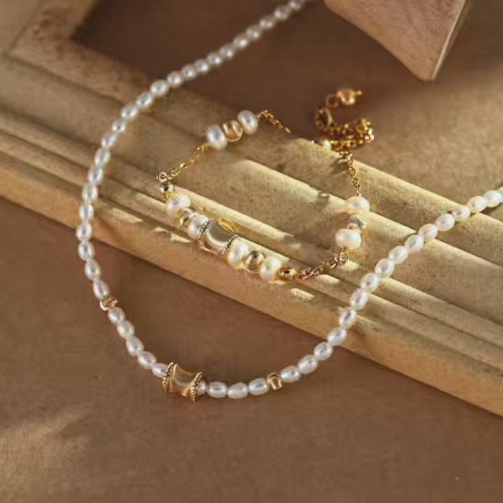 Dainty gold-plated freshwater pearl bracelet with polished beads and a curved centre charm, displayed beside a coordinating pearl necklace on a vintage-style tray.